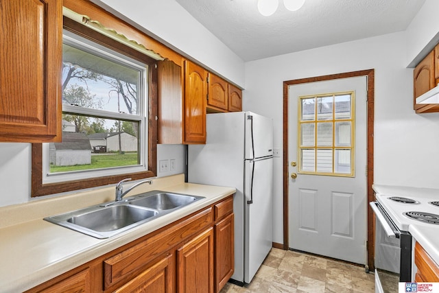 kitchen featuring brown cabinets, a sink, white appliances, light countertops, and stone finish floor