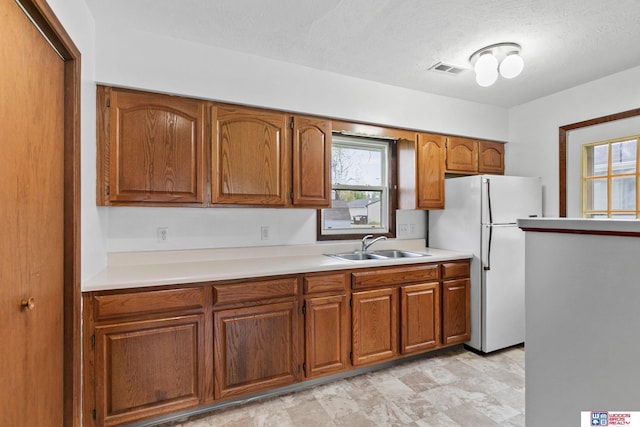 kitchen with freestanding refrigerator, brown cabinetry, a sink, and light countertops