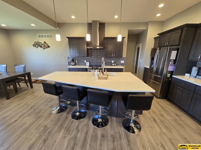 kitchen with stainless steel fridge with ice dispenser, light countertops, visible vents, wall chimney exhaust hood, and a sink