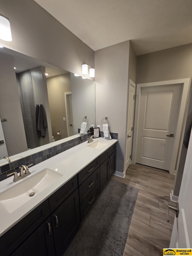 bathroom featuring tasteful backsplash, wood finished floors, double vanity, and a sink