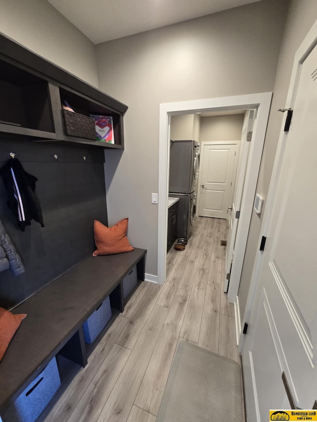 mudroom featuring light wood-style flooring, stacked washing maching and dryer, and baseboards