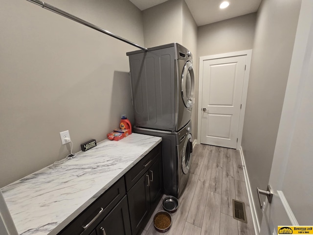 washroom featuring light wood-style flooring, visible vents, stacked washer / dryer, baseboards, and cabinet space