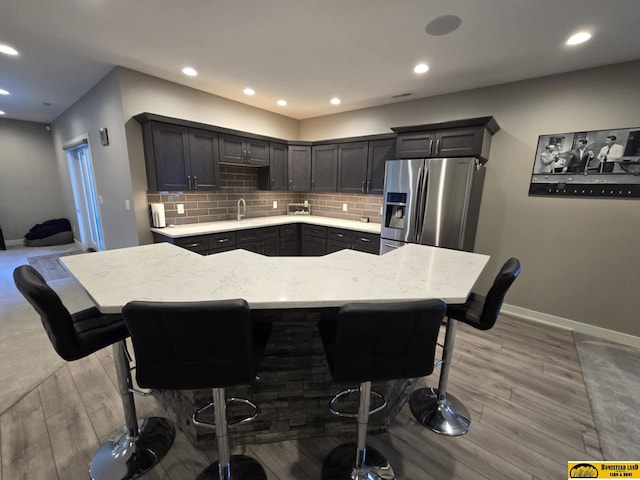 kitchen featuring stainless steel fridge with ice dispenser, tasteful backsplash, light wood-type flooring, and a sink