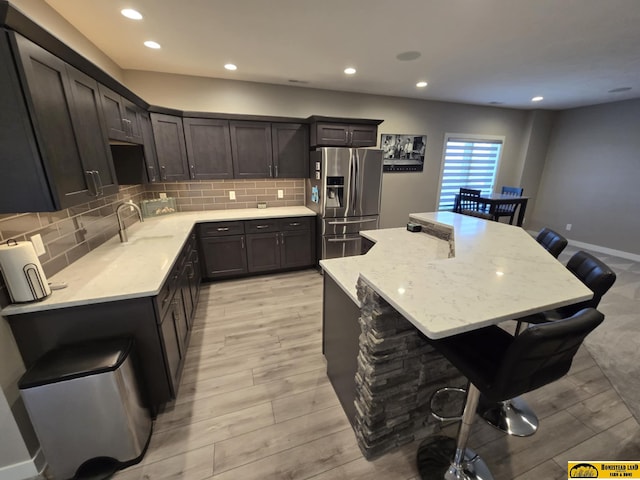 kitchen with light wood-type flooring, a kitchen island, recessed lighting, stainless steel refrigerator with ice dispenser, and backsplash