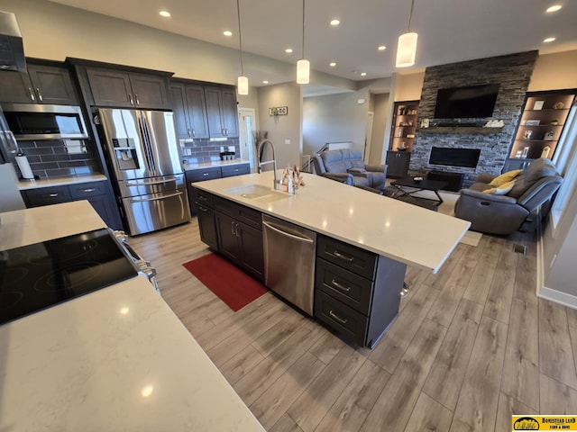 kitchen featuring a fireplace, appliances with stainless steel finishes, a sink, open floor plan, and light wood finished floors