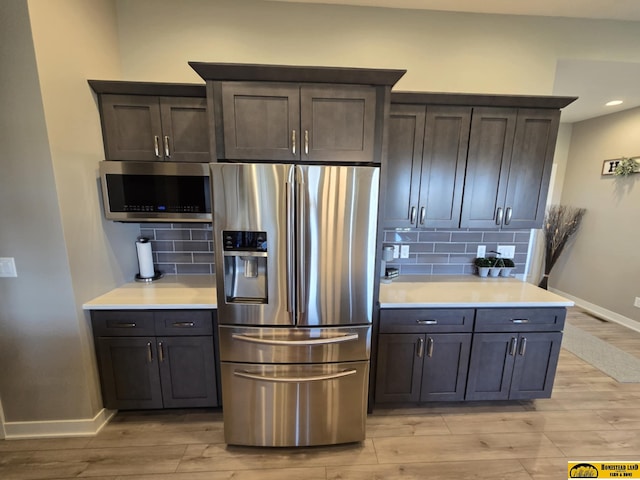 kitchen featuring light wood-type flooring, light countertops, backsplash, and stainless steel appliances