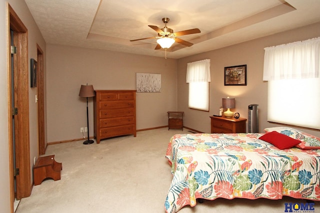 carpeted bedroom featuring a tray ceiling, baseboards, and a ceiling fan