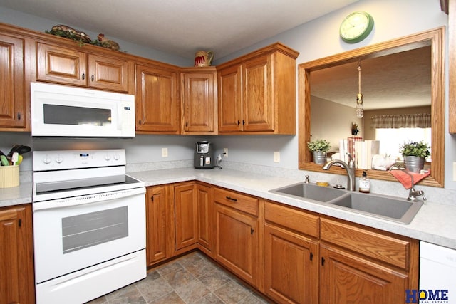 kitchen featuring light countertops, a sink, white appliances, and brown cabinetry