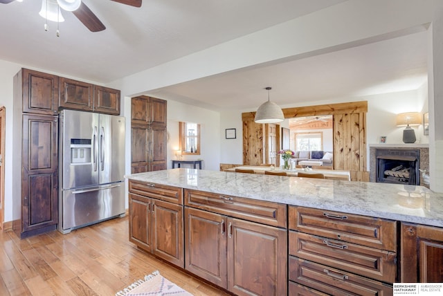 kitchen featuring ceiling fan, light stone countertops, stainless steel fridge, open floor plan, and light wood finished floors