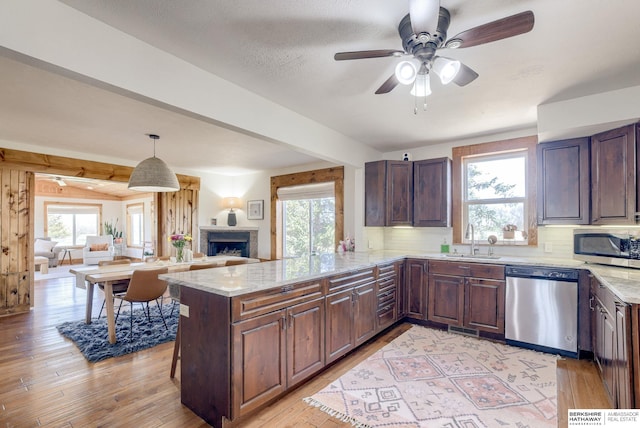 kitchen featuring a fireplace, appliances with stainless steel finishes, a sink, open floor plan, and light wood finished floors