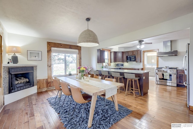 dining room featuring a textured ceiling, a ceiling fan, light wood-style floors, and a fireplace