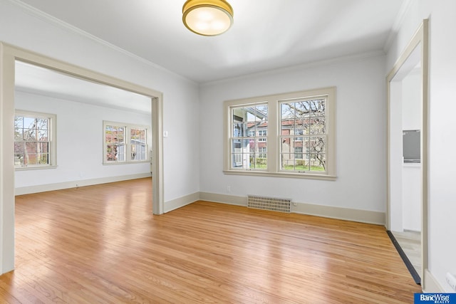 spare room with light wood finished floors, baseboards, ornamental molding, and visible vents