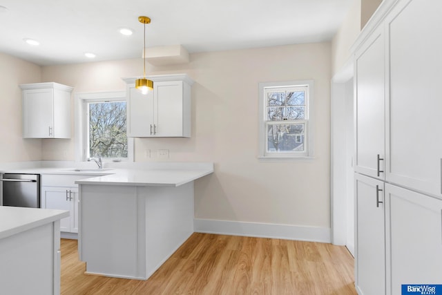 kitchen with baseboards, light countertops, white cabinets, dishwasher, and a sink