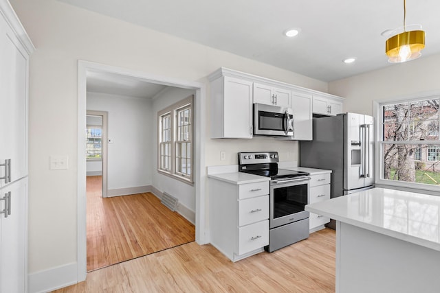 kitchen with light wood-style flooring, light countertops, white cabinetry, and appliances with stainless steel finishes