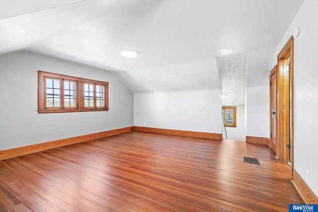 additional living space with hardwood / wood-style floors, visible vents, baseboards, and vaulted ceiling