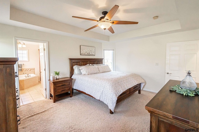 bedroom with a tray ceiling, ensuite bath, light colored carpet, and ceiling fan