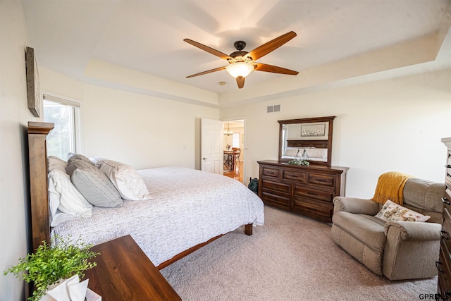 carpeted bedroom with ceiling fan, a tray ceiling, and visible vents