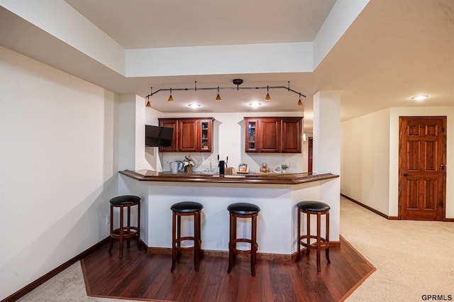 kitchen with dark countertops, baseboards, a kitchen bar, glass insert cabinets, and track lighting