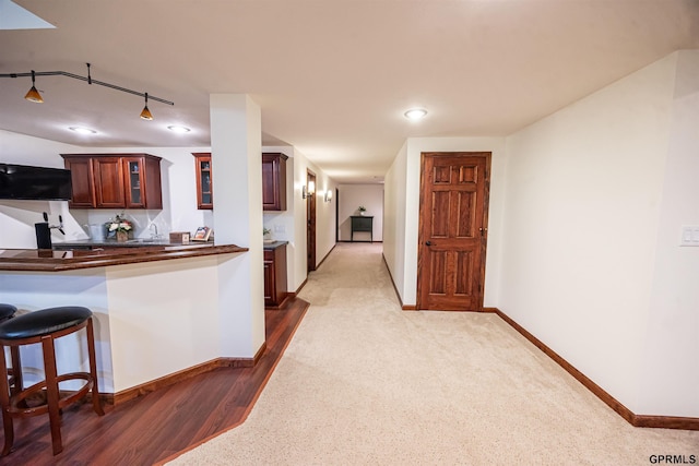 kitchen with dark countertops, glass insert cabinets, rail lighting, baseboards, and dark colored carpet