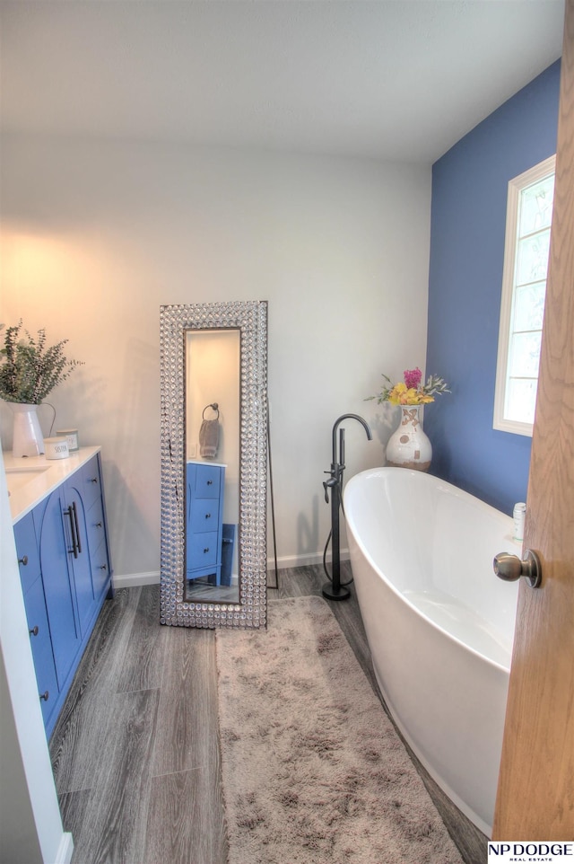 full bath with wood finished floors, vanity, a freestanding bath, and baseboards