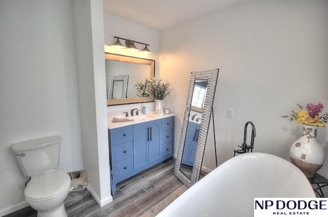 bathroom with a soaking tub, baseboards, toilet, wood finished floors, and vanity