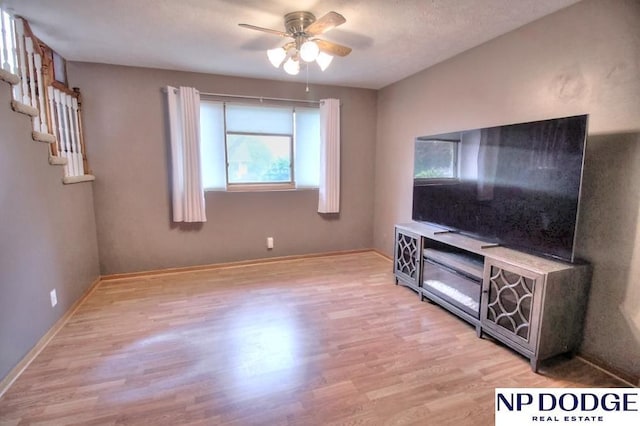 unfurnished living room featuring baseboards, ceiling fan, stairs, and light wood finished floors