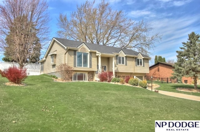 bi-level home featuring a garage, brick siding, fence, and a front yard