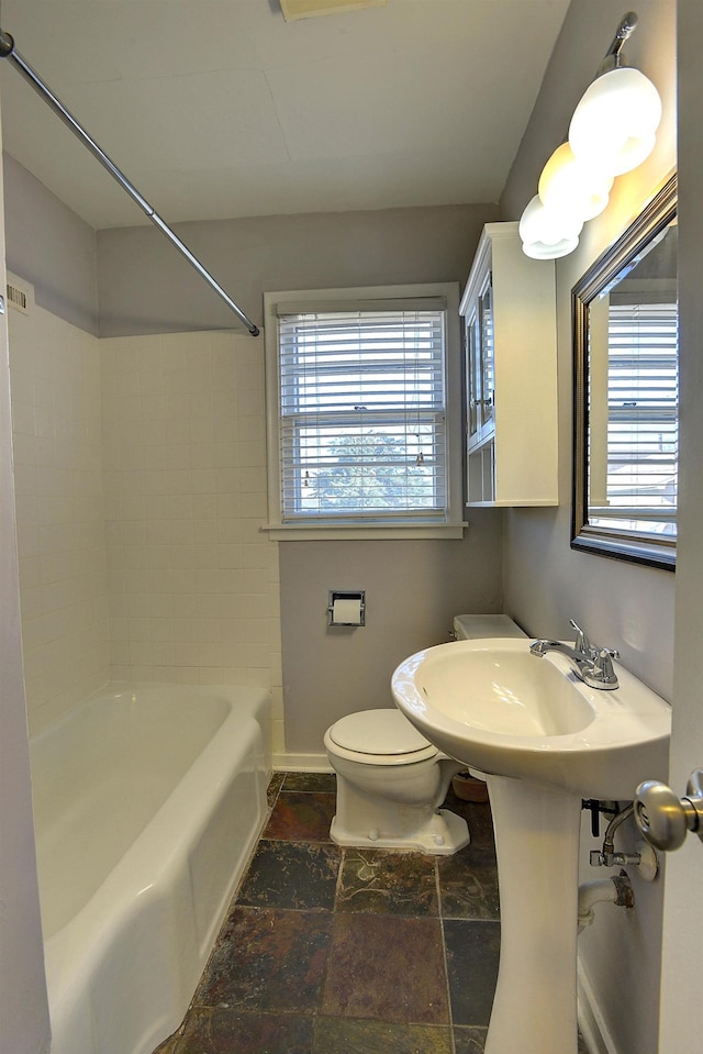 full bathroom with toilet, shower / tub combination, baseboards, and stone tile flooring