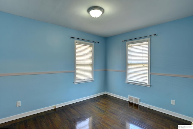 unfurnished room with dark wood-style flooring, visible vents, and baseboards