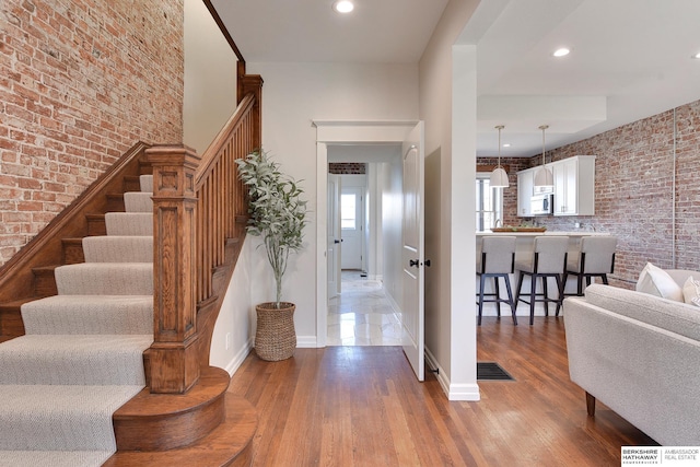 foyer entrance featuring brick wall, baseboards, and stairway