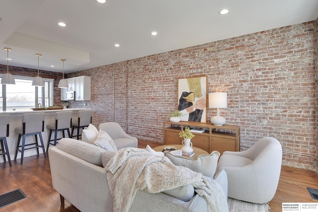 living room featuring visible vents, recessed lighting, wood finished floors, and brick wall