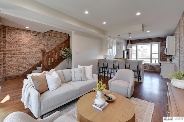 living area featuring dark wood-type flooring, recessed lighting, brick wall, and stairs