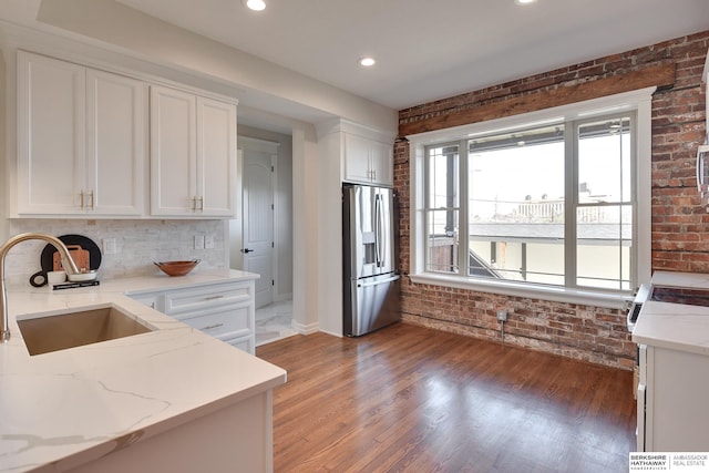 kitchen with brick wall, white cabinetry, a sink, and stainless steel fridge