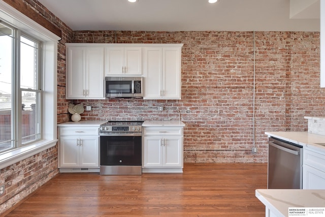 kitchen featuring stainless steel appliances, a wealth of natural light, brick wall, and white cabinets
