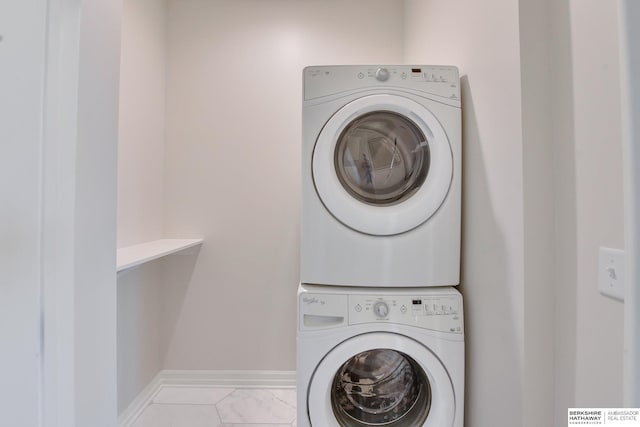 washroom featuring marble finish floor, baseboards, and stacked washer / drying machine