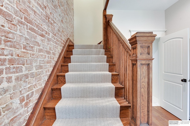 staircase with brick wall and wood finished floors