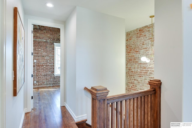 hall with brick wall, wood finished floors, baseboards, and an upstairs landing