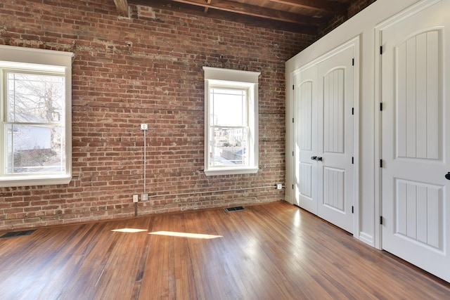 unfurnished bedroom with visible vents, beam ceiling, and brick wall