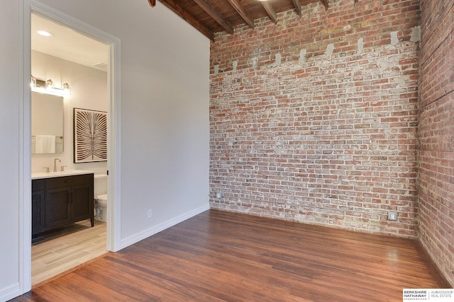 unfurnished room with baseboards, brick wall, visible vents, a sink, and wood finished floors