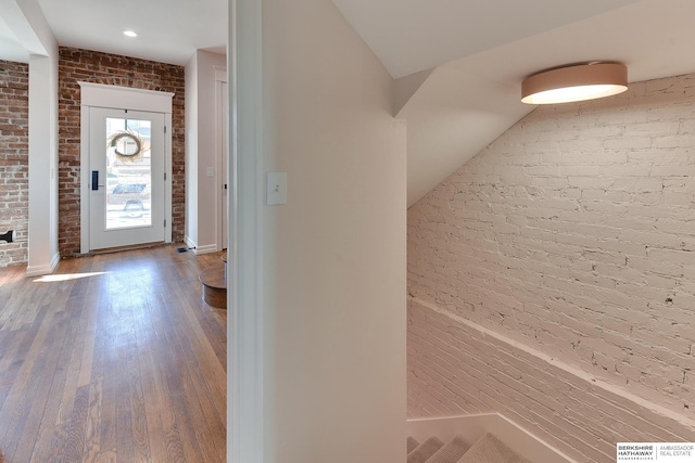foyer featuring baseboards, wood finished floors, and brick wall