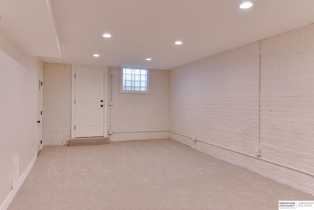 below grade area with visible vents, recessed lighting, light colored carpet, and brick wall