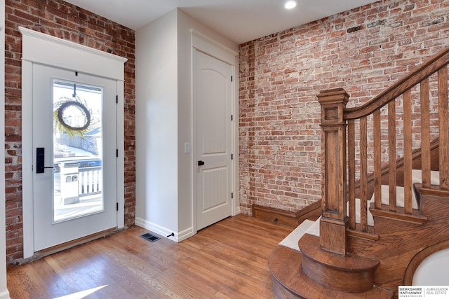 foyer entrance featuring brick wall, wood finished floors, baseboards, and visible vents
