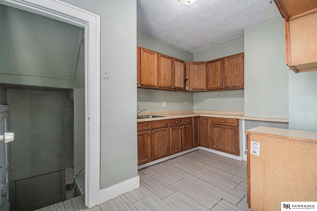 kitchen with brown cabinets, light countertops, baseboards, and a sink