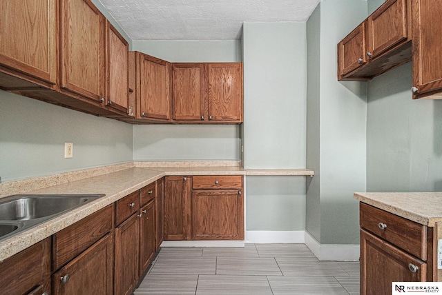 kitchen featuring brown cabinets, a sink, light countertops, and baseboards