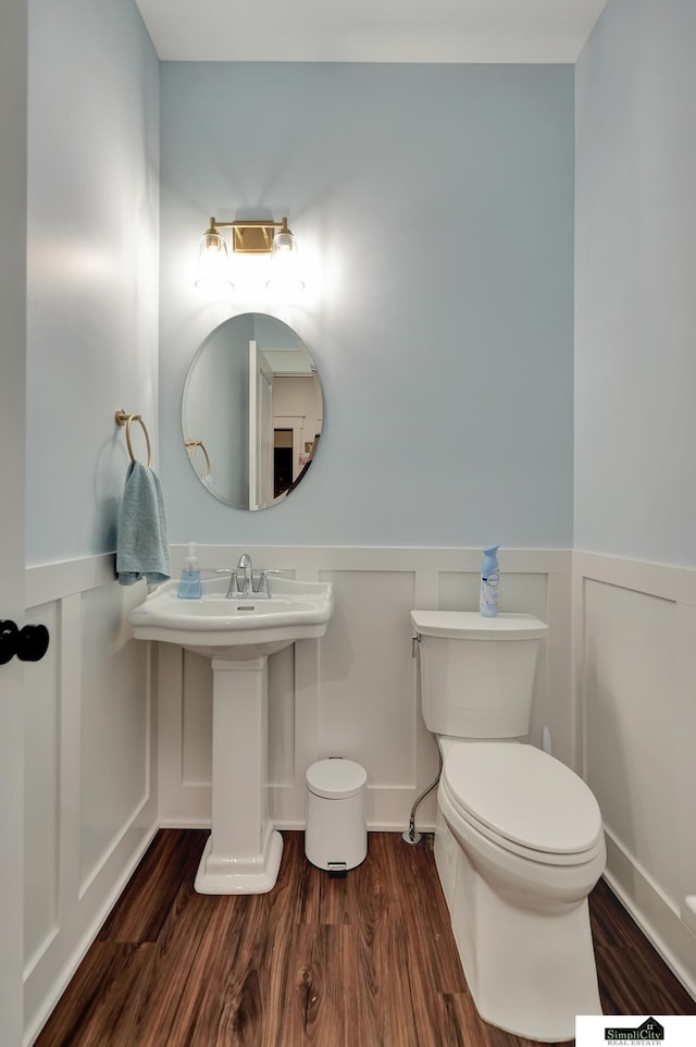 half bathroom featuring a decorative wall, a wainscoted wall, and wood finished floors