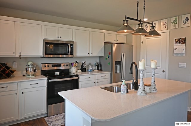 kitchen featuring white cabinets, a sink, appliances with stainless steel finishes, a center island with sink, and light stone counters