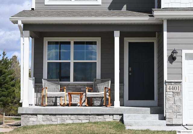 property entrance with a shingled roof, covered porch, and stone siding