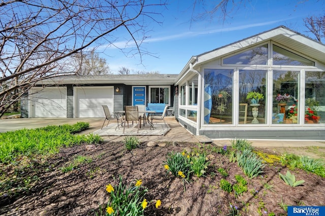 rear view of house featuring a garage, a patio, a sunroom, and concrete driveway