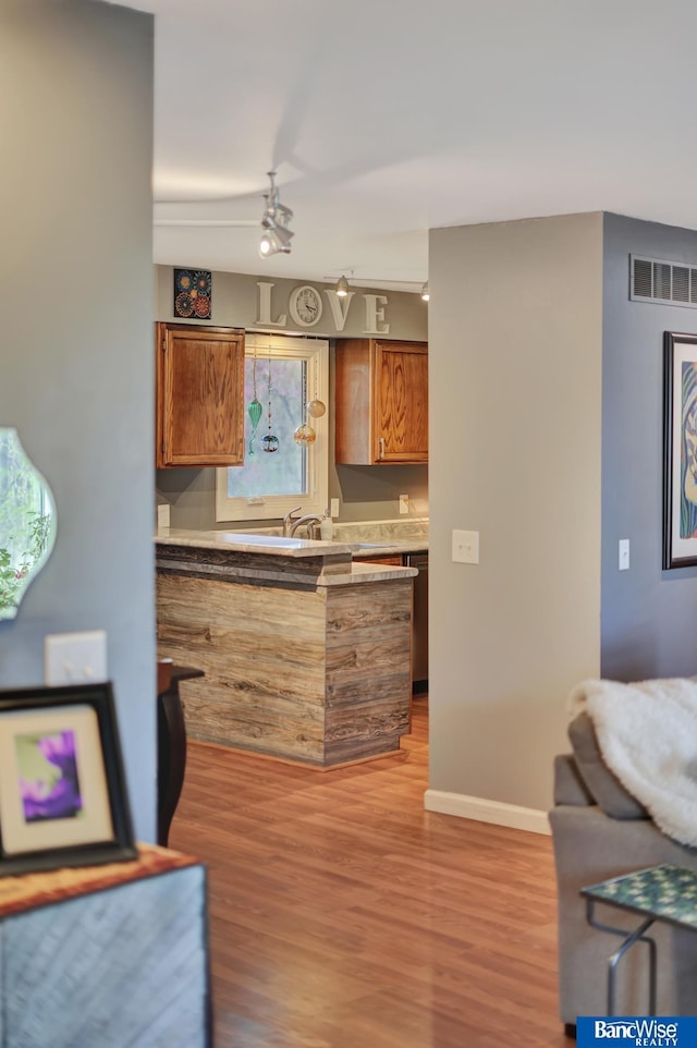 kitchen with baseboards, a peninsula, visible vents, brown cabinets, and light wood finished floors