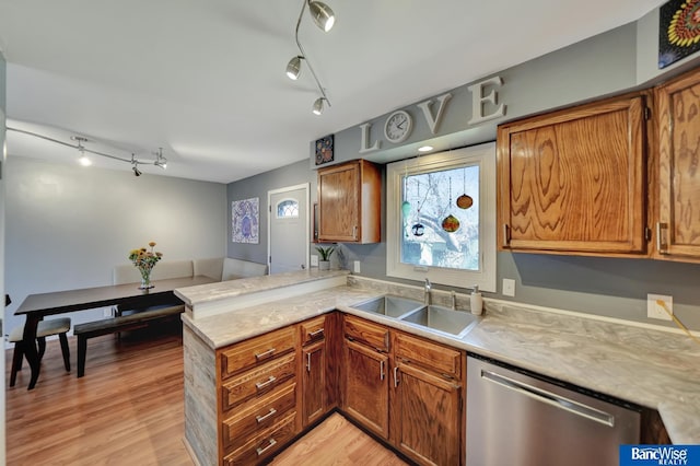 kitchen featuring stainless steel dishwasher, track lighting, a peninsula, light countertops, and a sink
